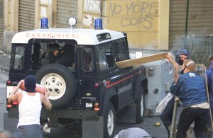 A CARABINIERE POINTS A GUN AS A PROTESTER TRIES TO HURL A FIRE EXTINQUISHER INTO THEIR VEHICLE